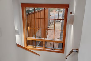 Ein Fenster mit Holzrahmen und mehreren Scheiben, das auf einen Garten mit Holzterrasse und einem Baum blickt.
