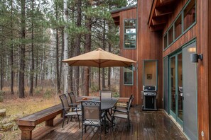 Een houten terras met een tafel, stoelen, een bank en een barbecue.