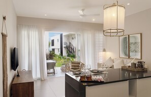 A modern living room with a central island, a flat-screen TV mounted on the wall, and a dining area with outdoor views. - O'biches by Horizon Holidays (Trou aux Biches)