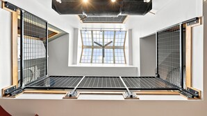 Een kamer met dakraam, metalen roosters en een plafond met zichtbare balken en verlichtingsarmaturen.