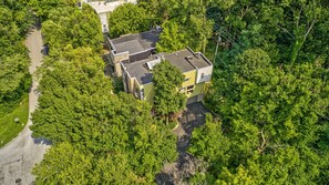 A two-story building surrounded by dense greenery, with a paved driveway leading to the entrance. - The Steele Mill | 4BR Modern Industrial Home (Indianapolis)