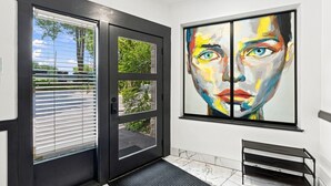 Una entrada moderna con puerta de cristal, un banco y un cuadro abstracto grande en la pared.
