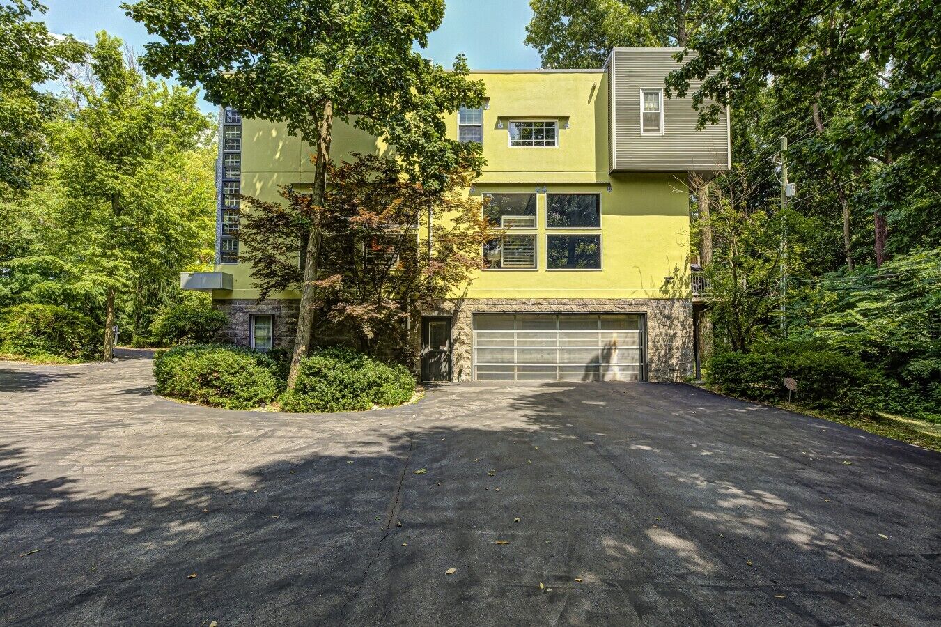 A two-story building with a garage, surrounded by trees and a driveway.