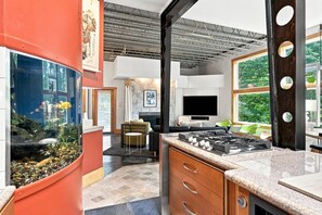 A modern kitchen with a built-in stove, a large fish tank, and a dining area with a fireplace. - The Steele Mill | 4BR Modern Industrial Home (Indianapolis)