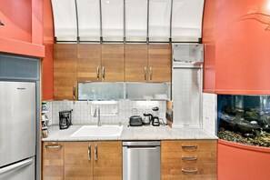 A kitchen with wooden cabinets, a stainless steel refrigerator, a dishwasher, and a built-in fish tank. - The Steele Mill | 4BR Modern Industrial Home (Indianapolis)