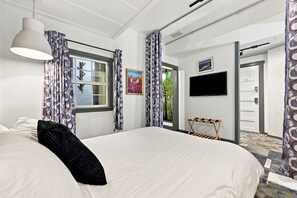 Habitación de hotel con una cama grande, un televisor montado en la pared, una ventana con cortinas y una puerta que da a un espacio al aire libre.