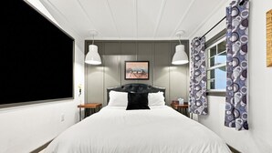 A hotel room with a large bed, two bedside tables, a wall-mounted TV, and a window with curtains.