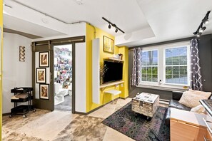Una sala de estar con televisor, sofá, mesa de centro y ventana con cortinas.