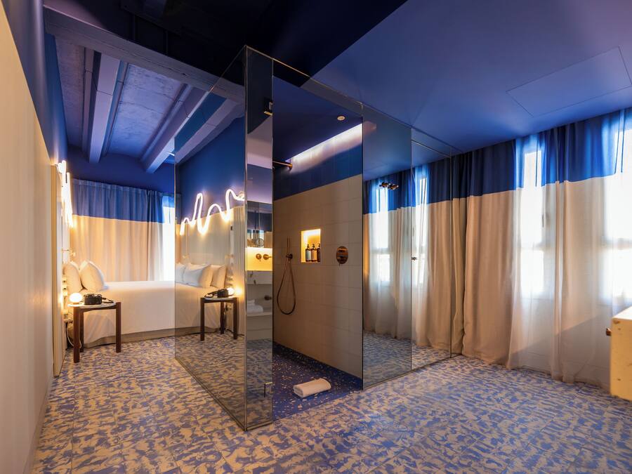 Habitación de hotel con cama, baño con ducha, espejo y suelo estampado.