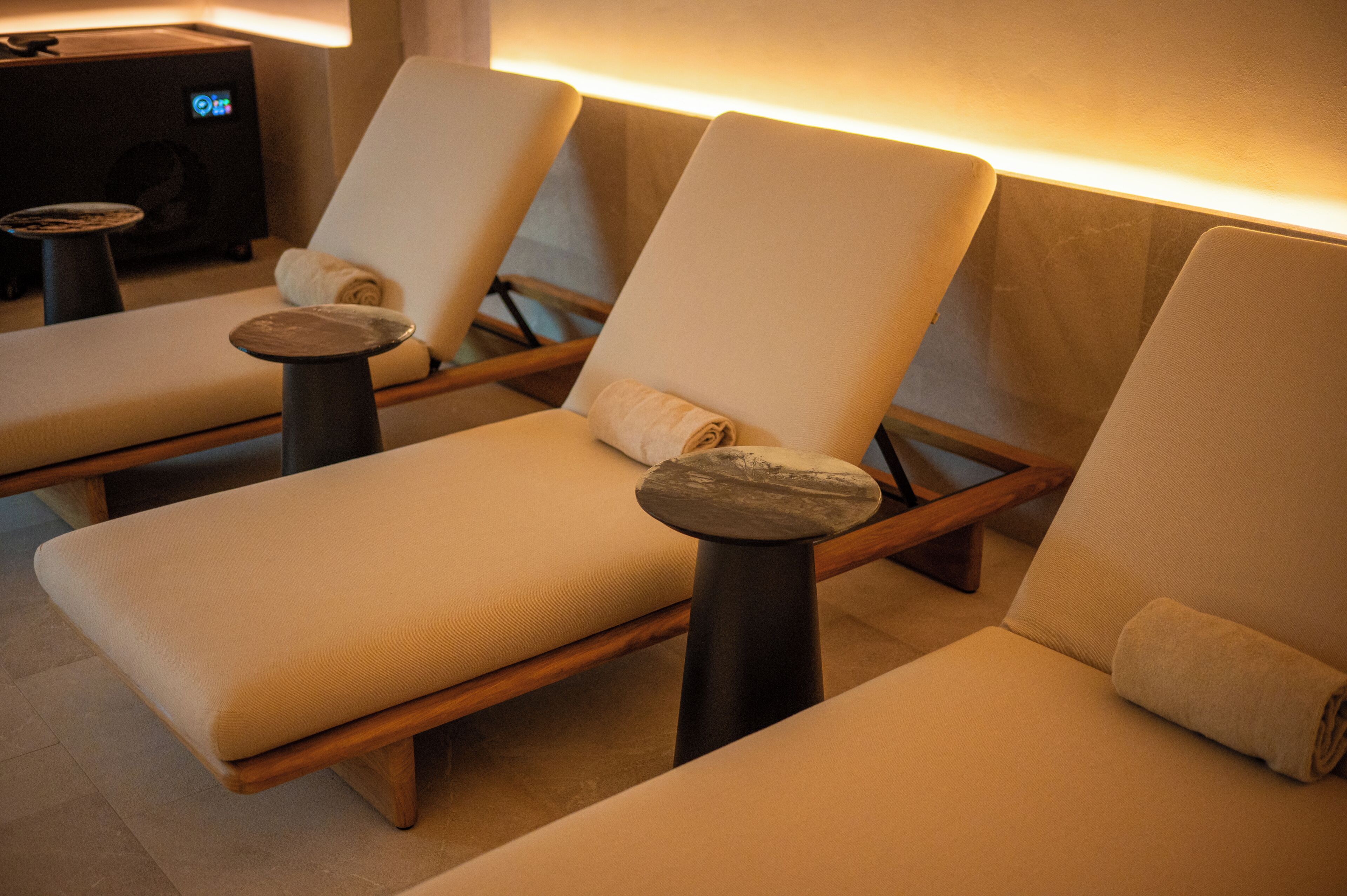 A spa room with three reclining chairs, each with a towel, and a massage table.