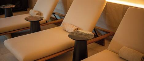 A spa room with three reclining chairs, each with a towel, and a massage table.