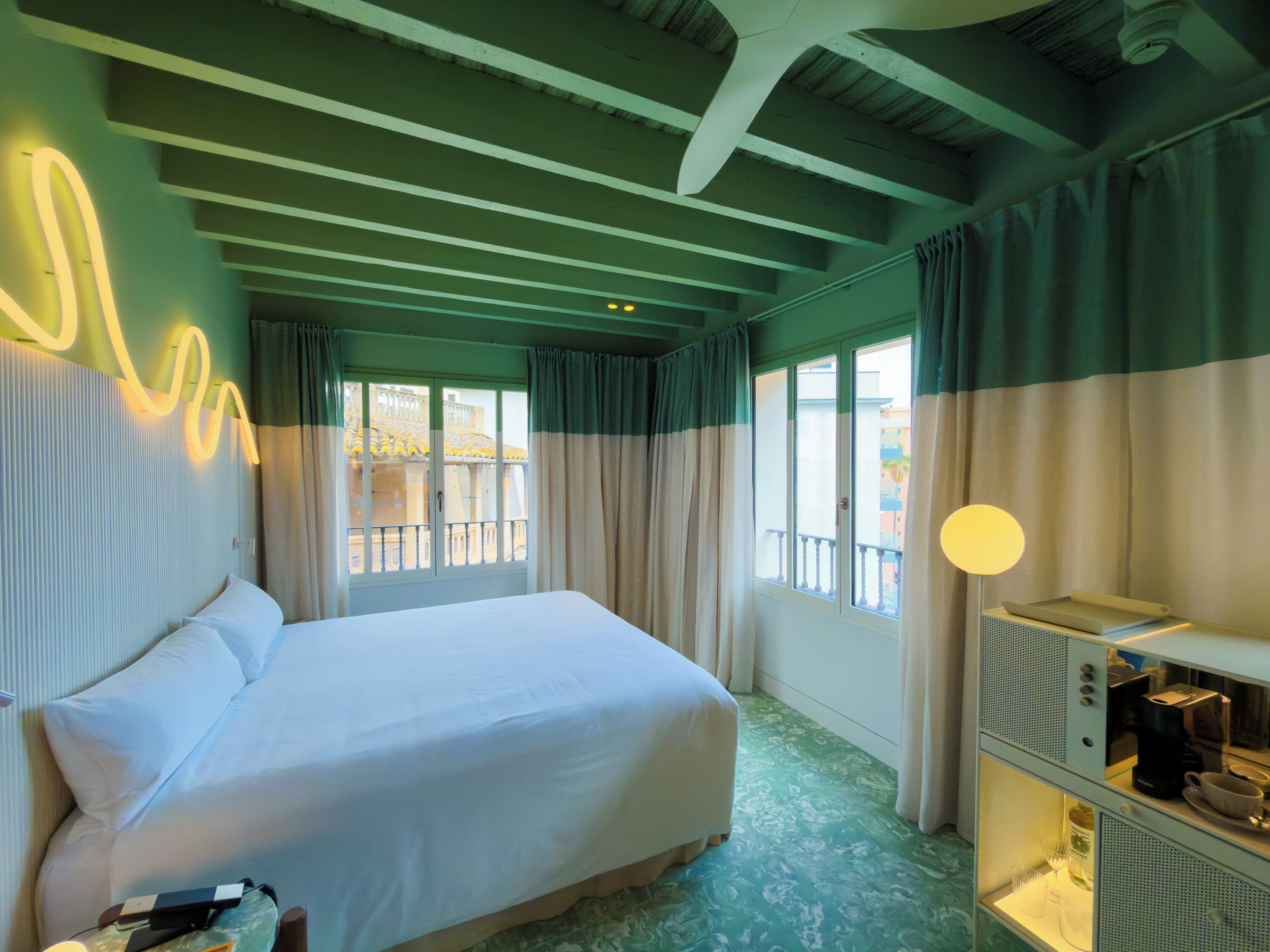 Una habitación de hotel con cama, escritorio con lámpara y vistas al exterior.