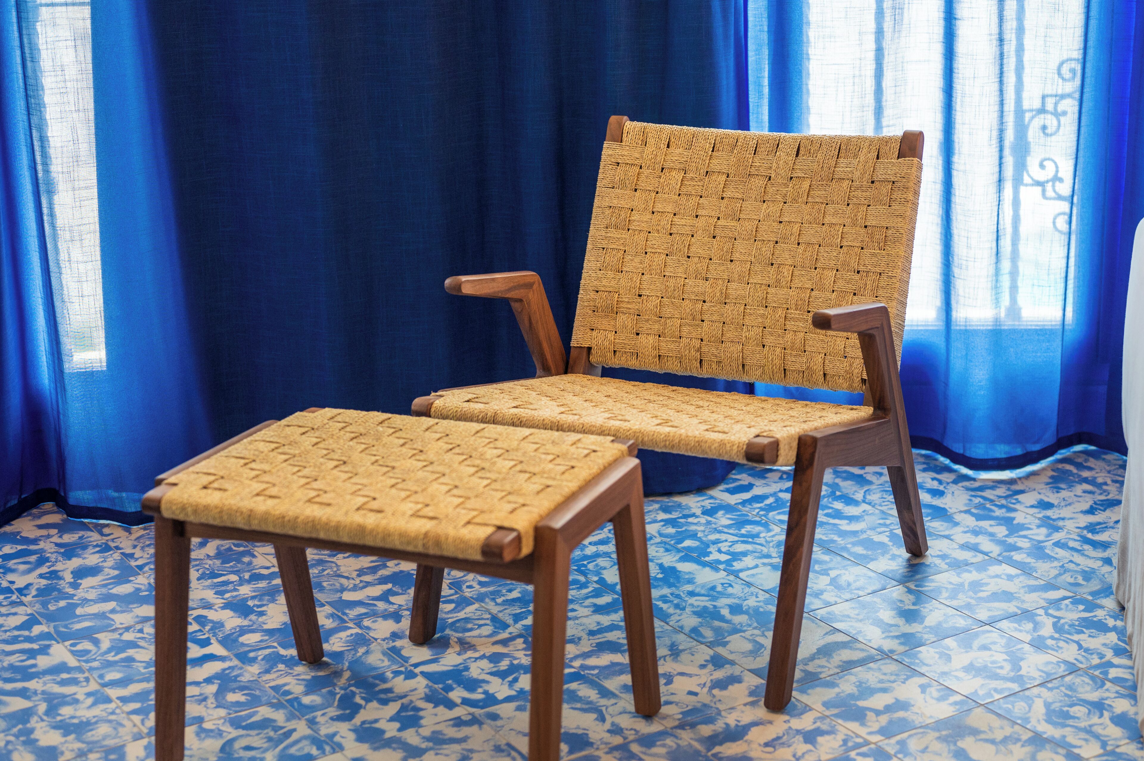 Una silla con respaldo y asiento tejido, patas de madera y un otoman a juego.