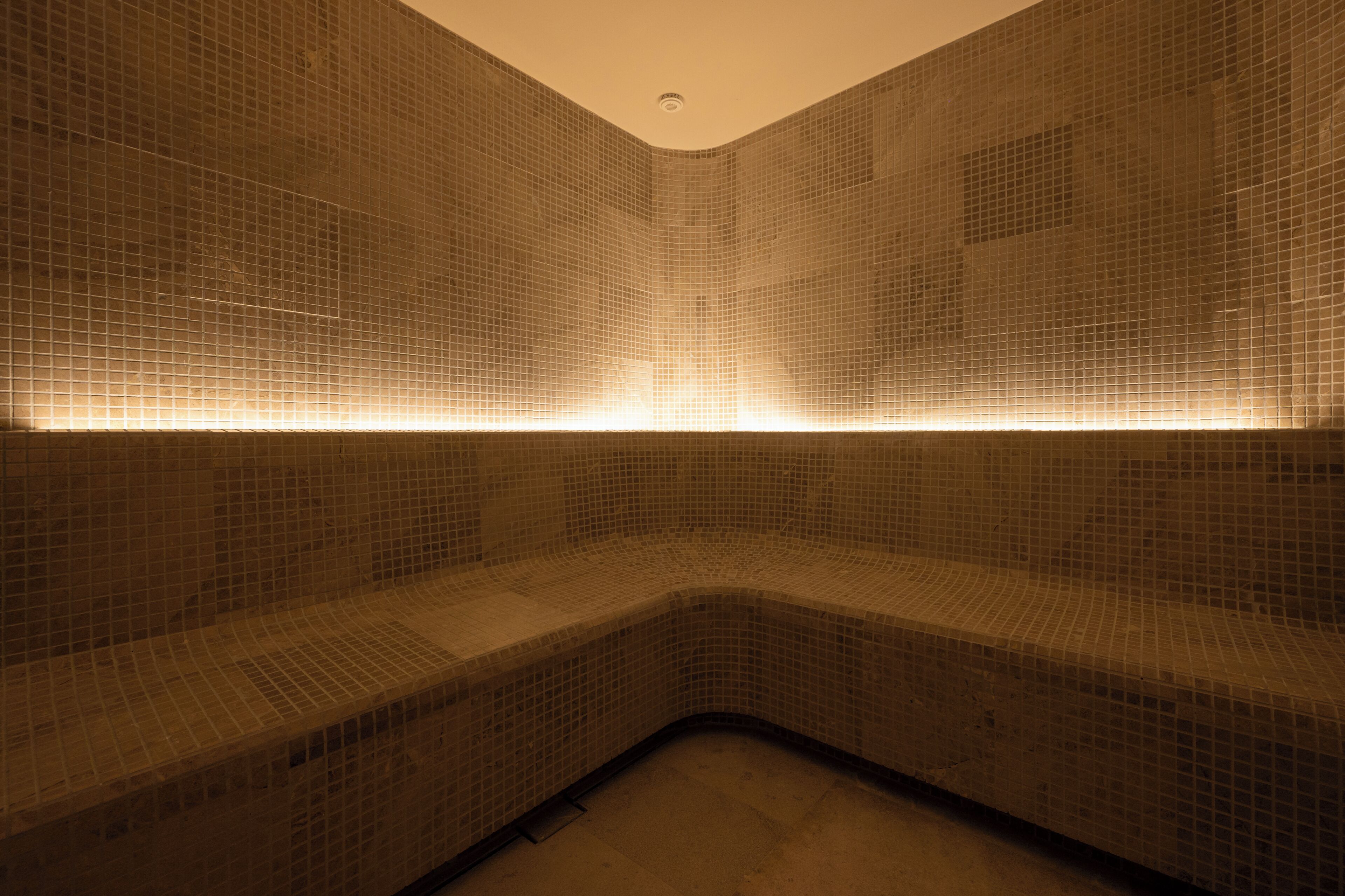 A corner of a room with tiled walls and a bench.