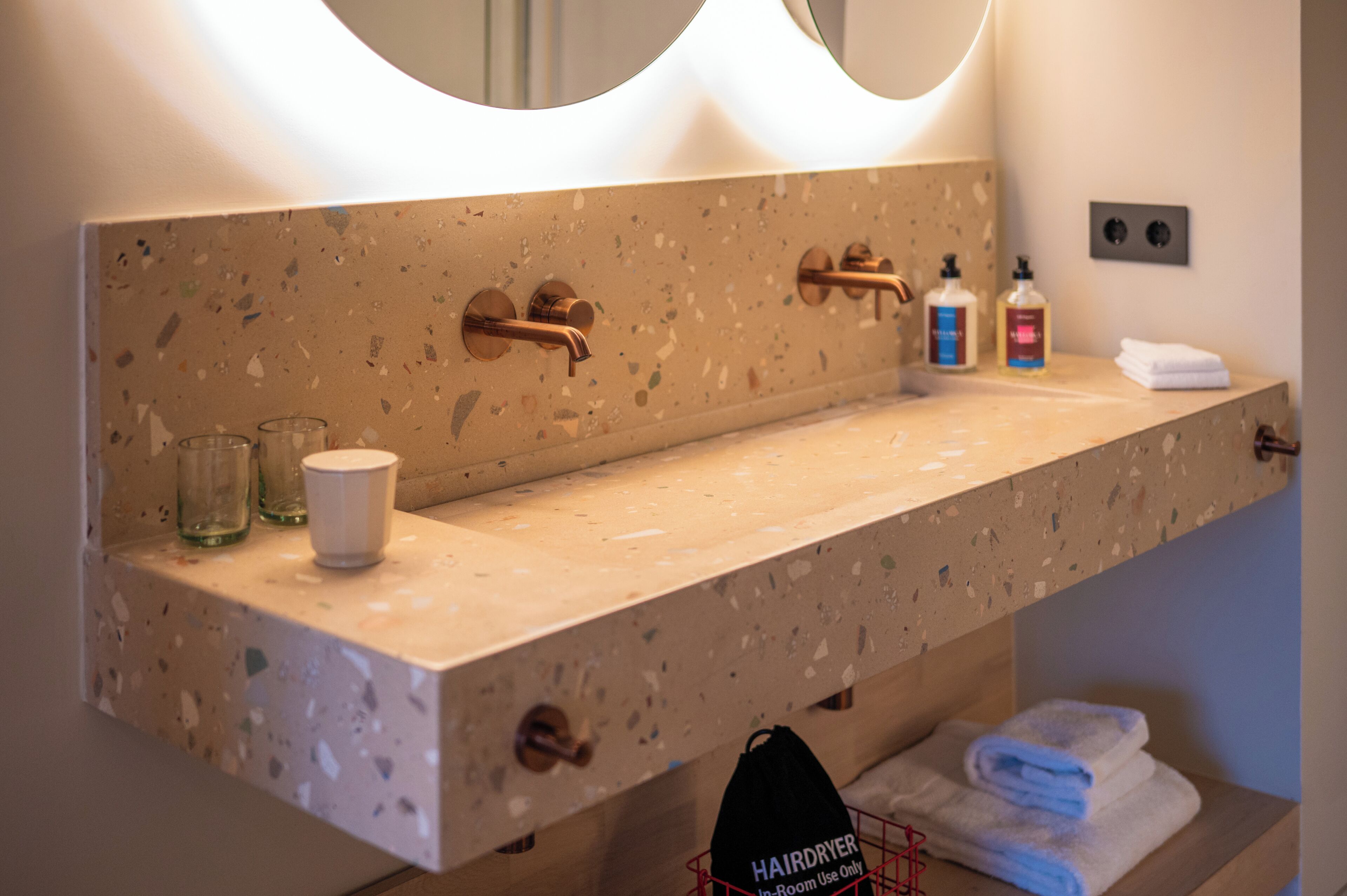 A bathroom with a terrazzo countertop, a mirror, a towel rack, and a hairdryer bag.