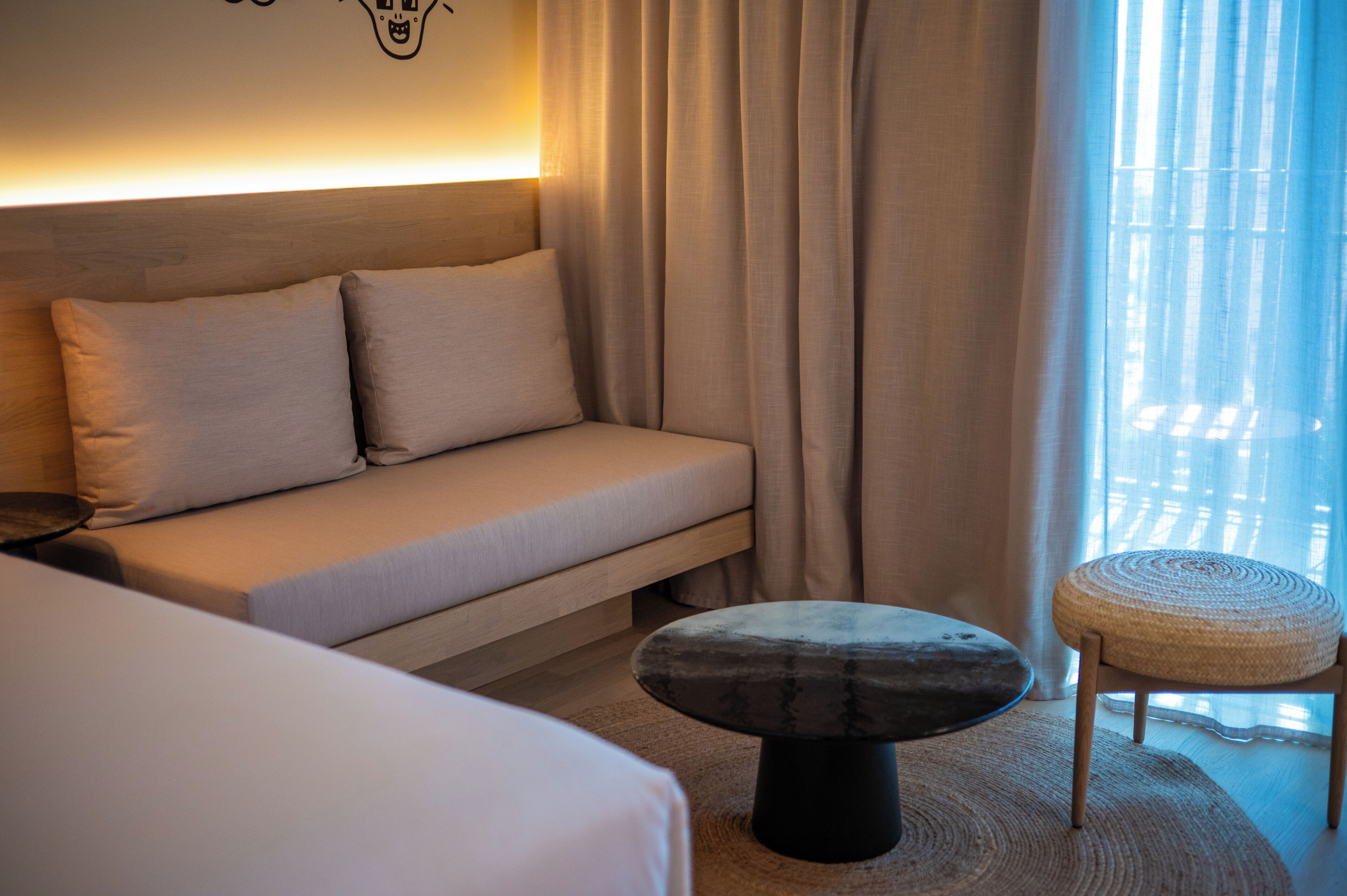 A modern hotel room with a sofa, a round ottoman, and a small table.
