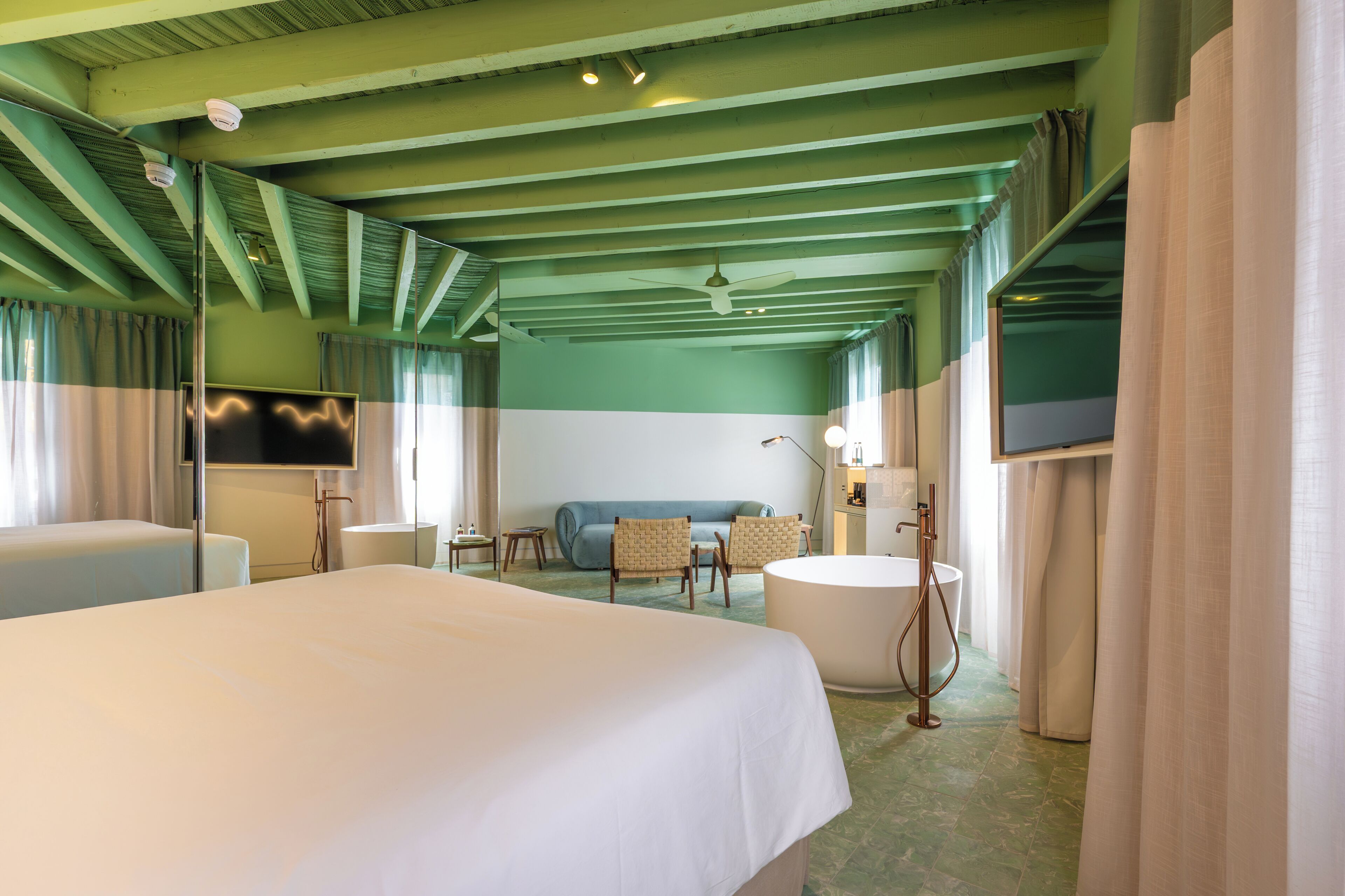 Una habitación de hotel con cama, sofá, bañera y televisor.