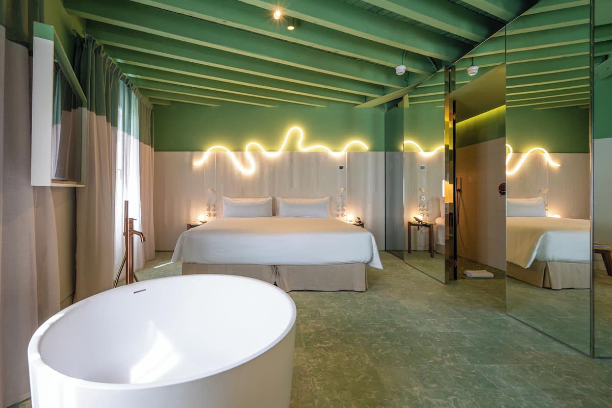 Habitación de hotel con una cama grande, una bañera y un espejo que refleja el espacio.