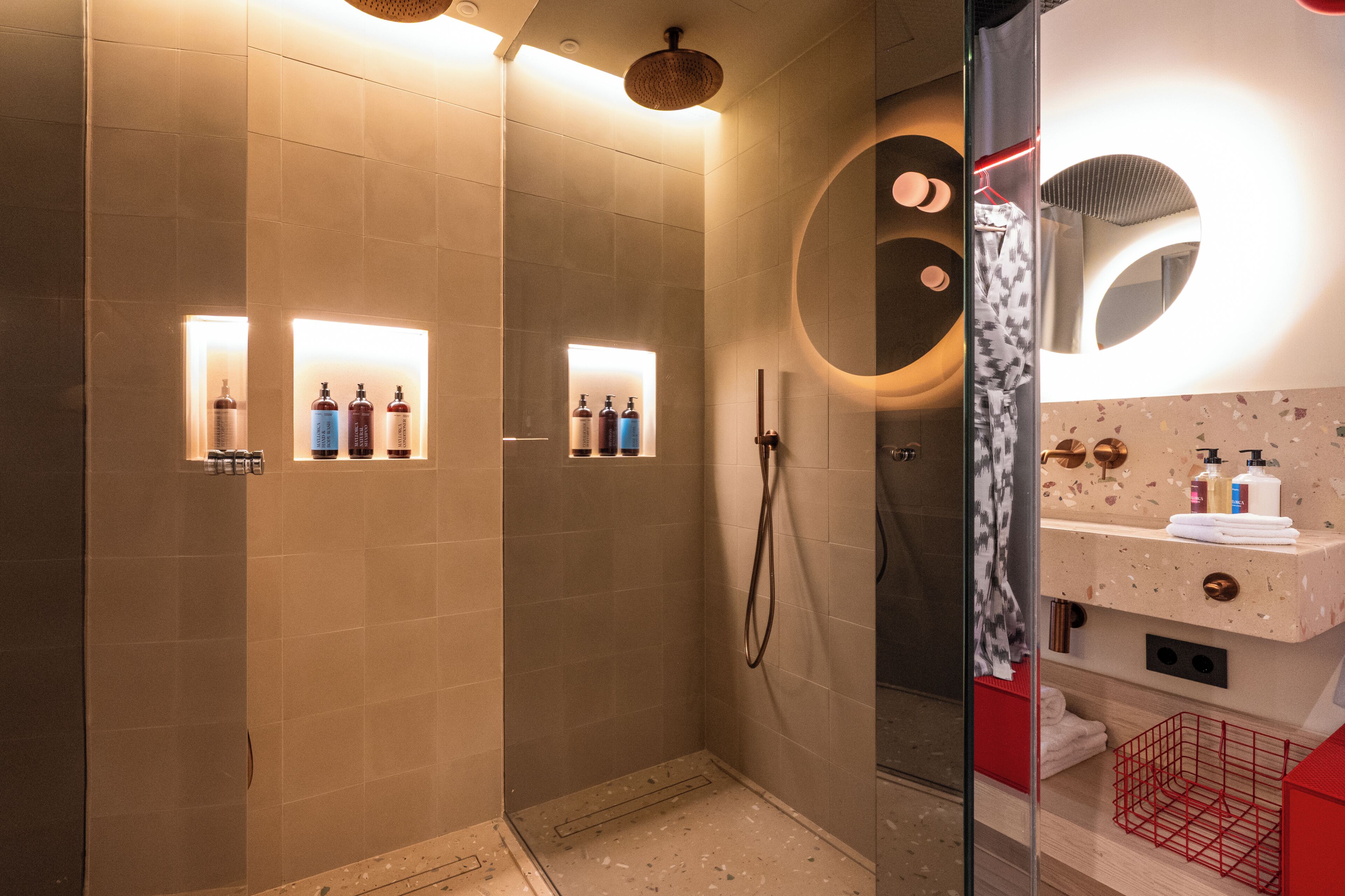 A modern bathroom with a glass-enclosed shower, a vanity with a mirror, and illuminated shelves with toiletries.