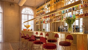 Zona de bar con varias estanterías llenas de botellas, taburetes rojos y un ventanal con cortinas.