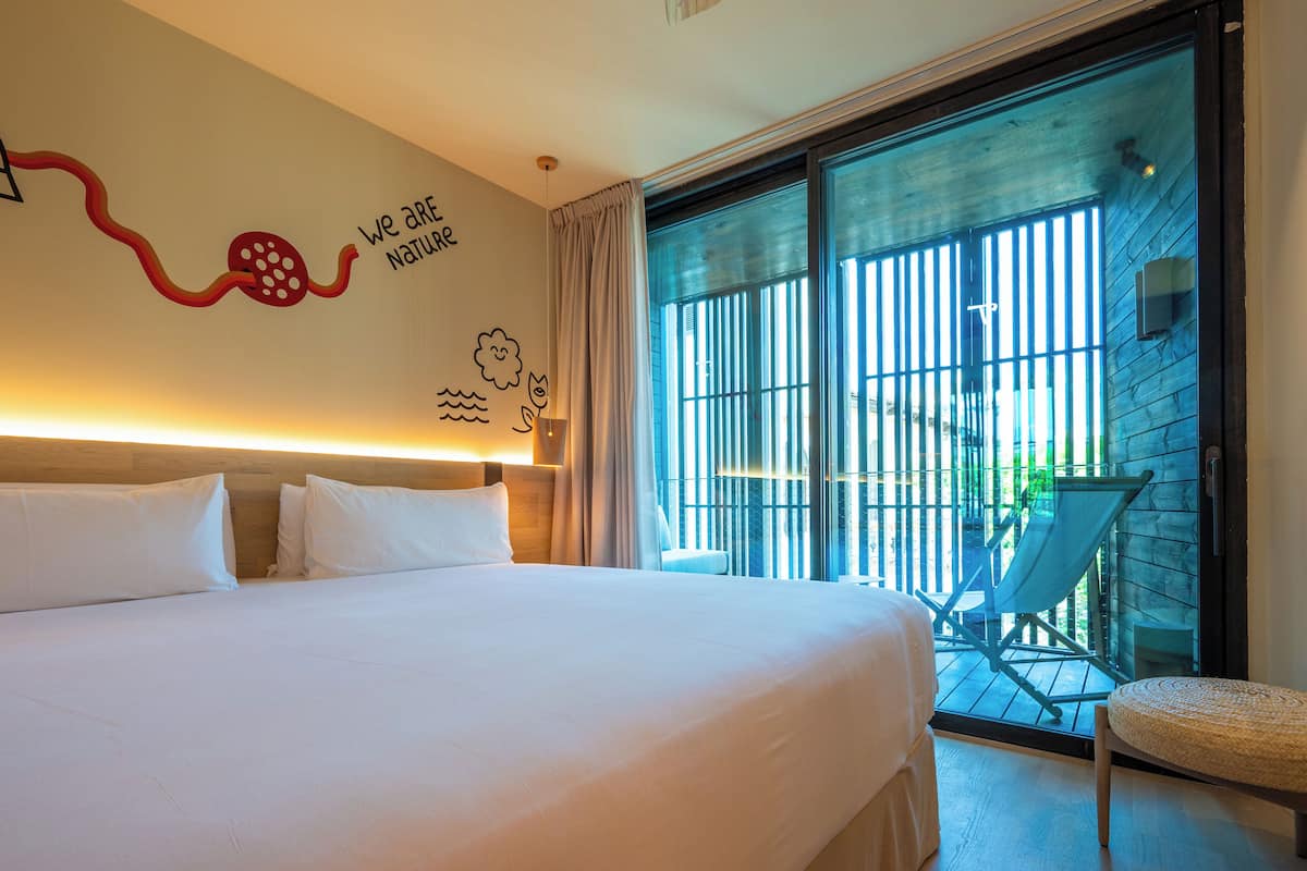 Una habitación de hotel con una cama grande, vistas al exterior y una silla junto a la ventana.