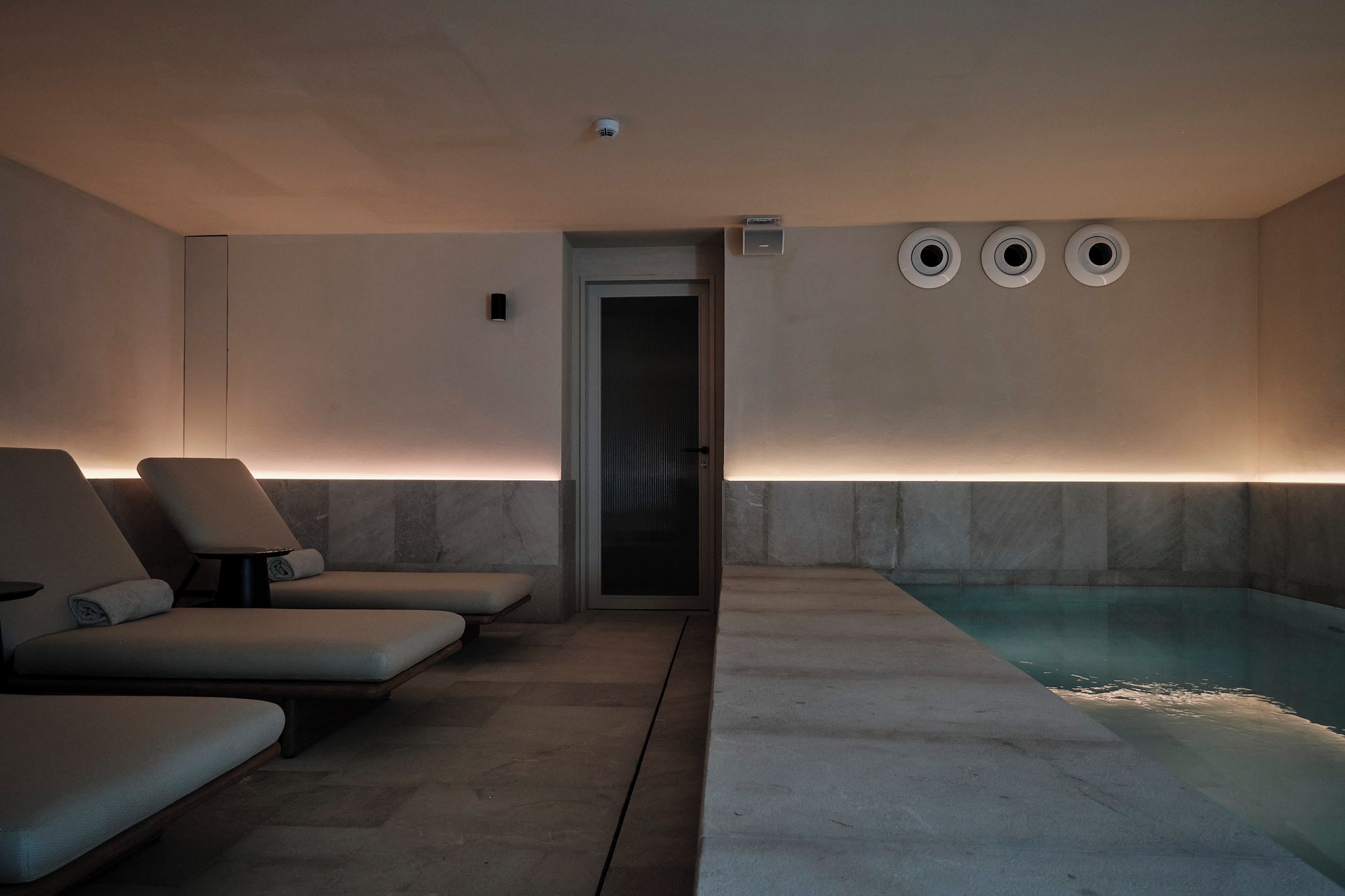 Un área de spa con piscina, sillas de descanso y una puerta que conduce a otra habitación.