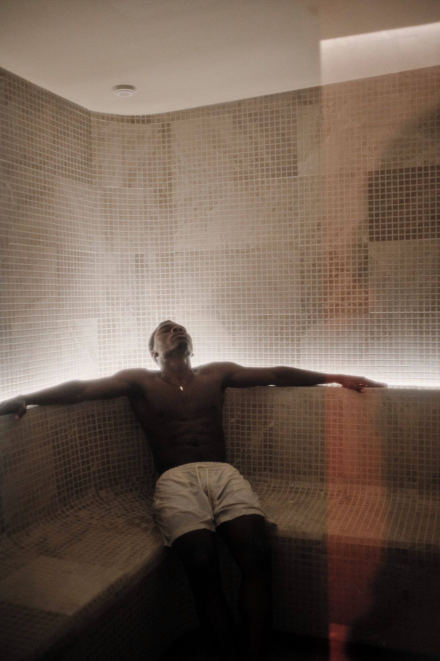 A person sitting on a tiled bench in a room with a tiled wall.