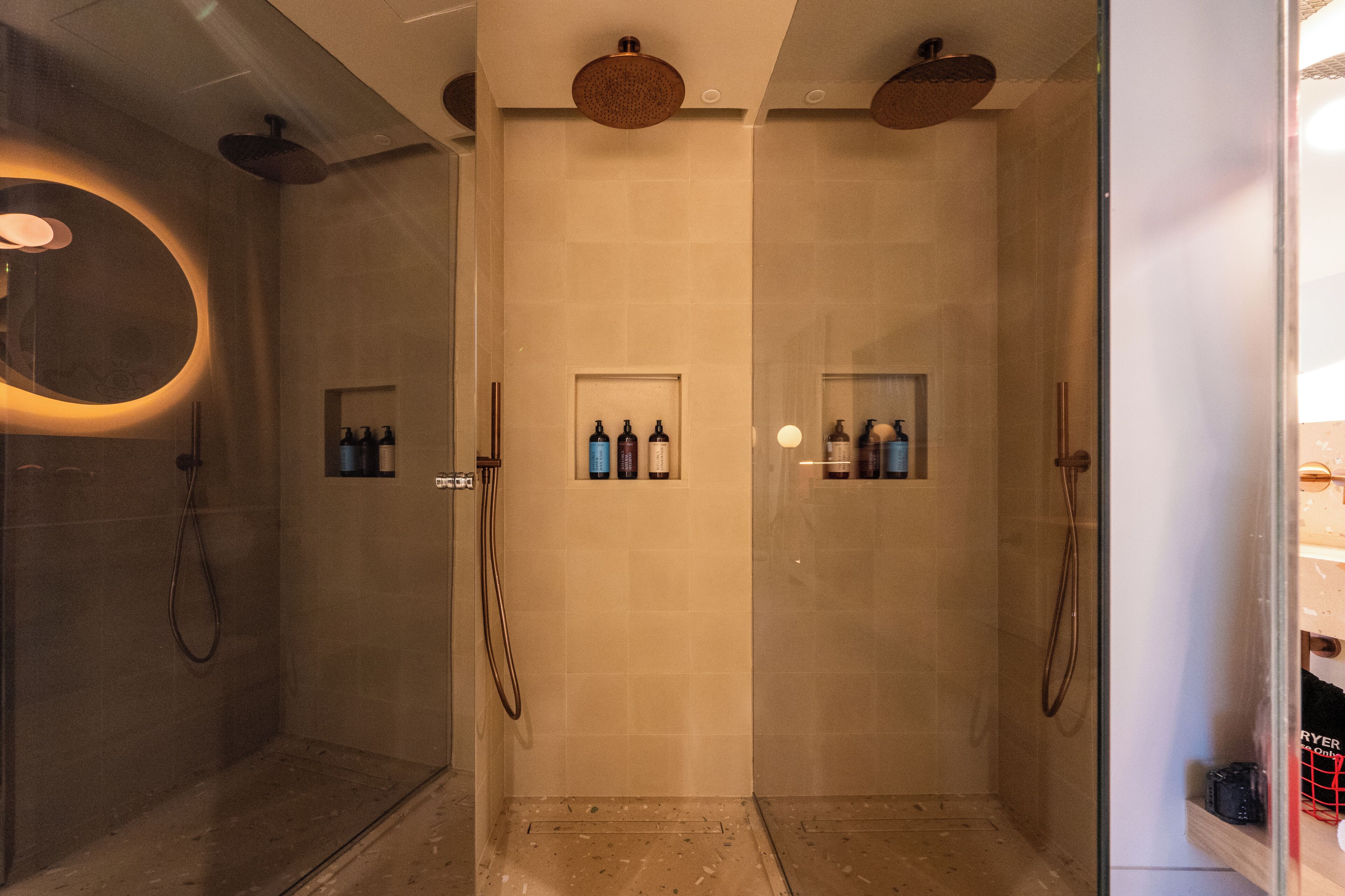 Un baño moderno con cabina de ducha de vidrio, un espejo redondo y dos estantes con artículos de aseo.