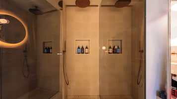 Un baño moderno con cabina de ducha de vidrio, un espejo redondo y dos estantes con artículos de aseo.
