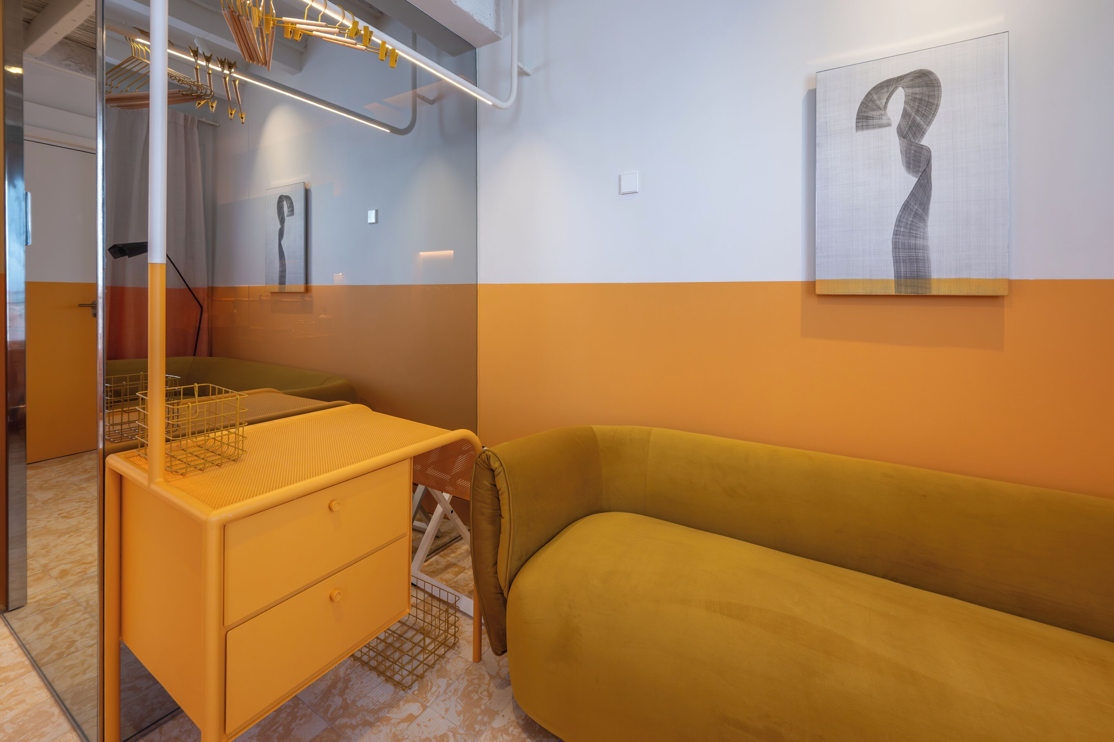 A modern room with a yellow sofa, a small wooden table, a metal rack, and a framed artwork on the wall.