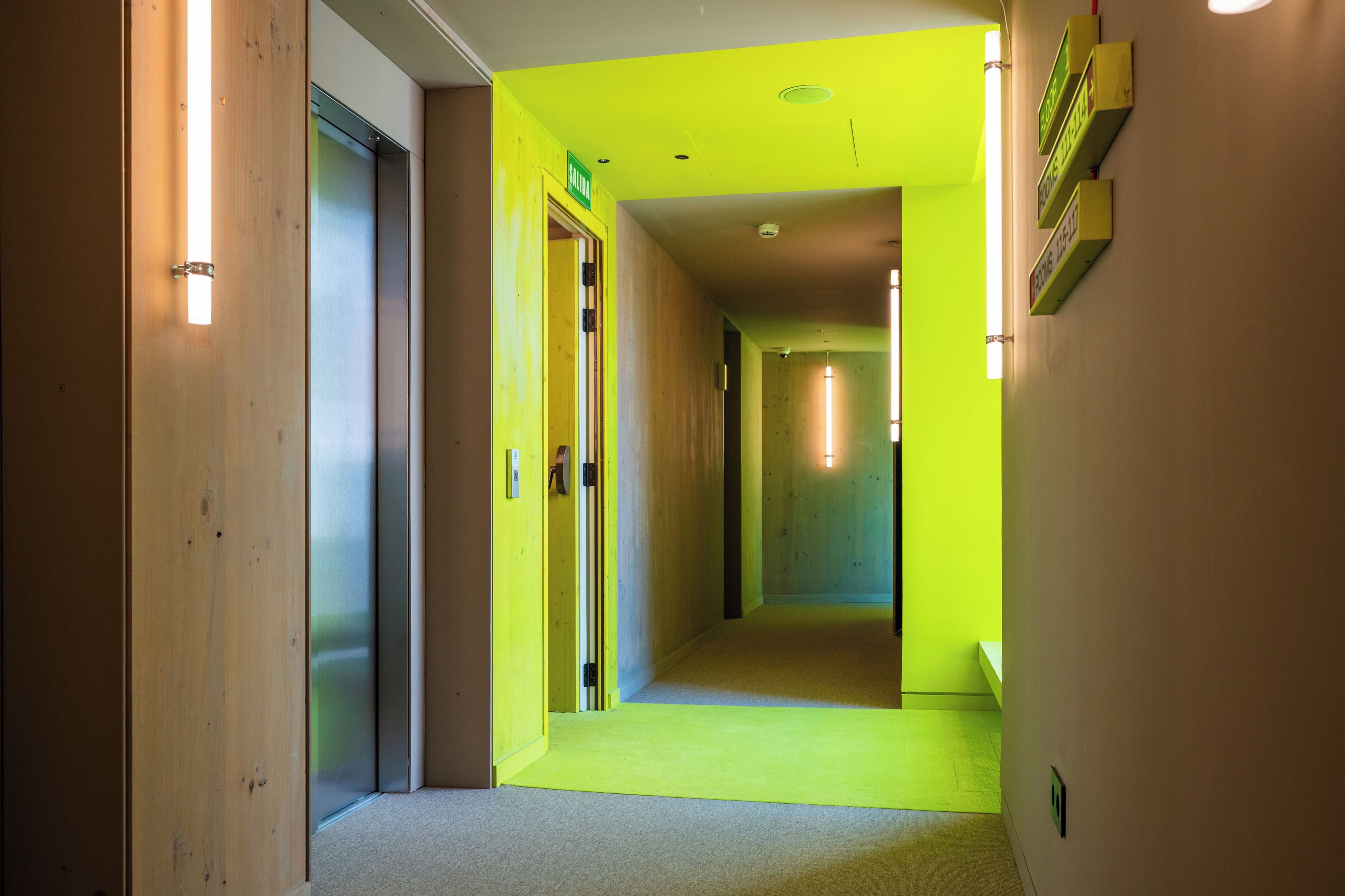 A hallway with a bright yellow carpet, wooden doors, and a wall-mounted sign.