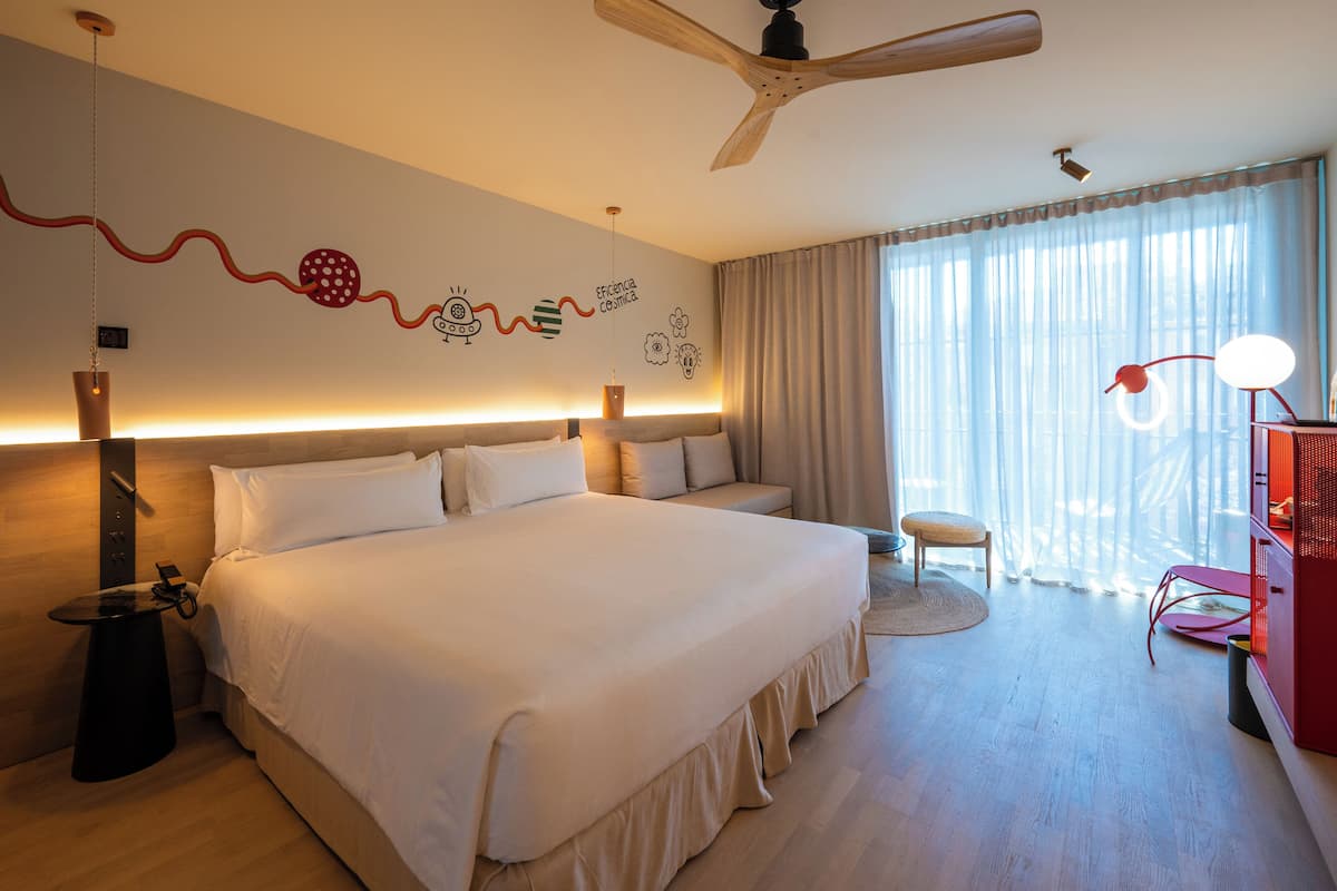 Una habitación de hotel con una cama grande, un ventilador de techo, un escritorio y una silla.