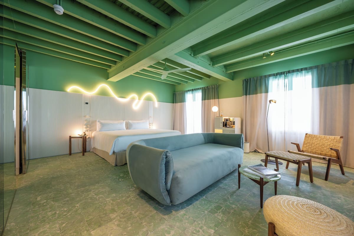 Una habitación con cama, sofá, sillón, lámpara y espejo.