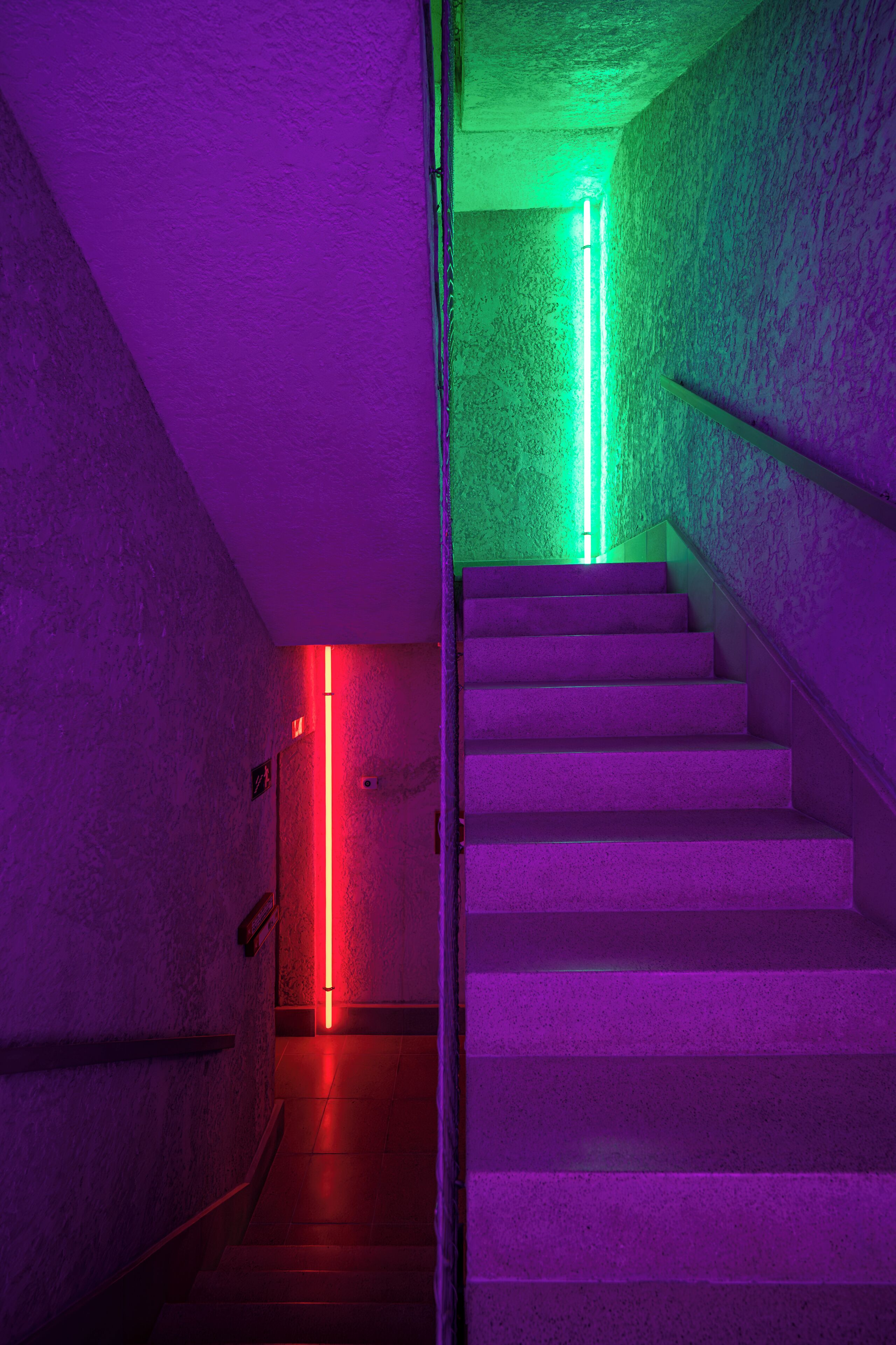 A staircase with a textured wall and a neon light.