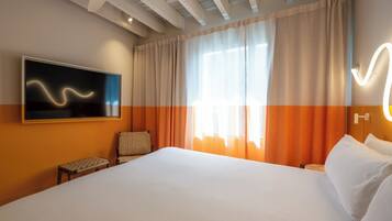 Une chambre d’hôtel avec un grand lit, un téléviseur fixé au mur, une chaise et une fenêtre avec des rideaux.