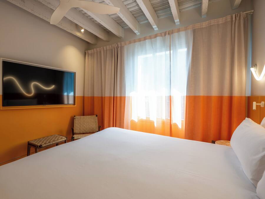 Une chambre d’hôtel avec un grand lit, un téléviseur fixé au mur, une chaise et une fenêtre avec des rideaux.