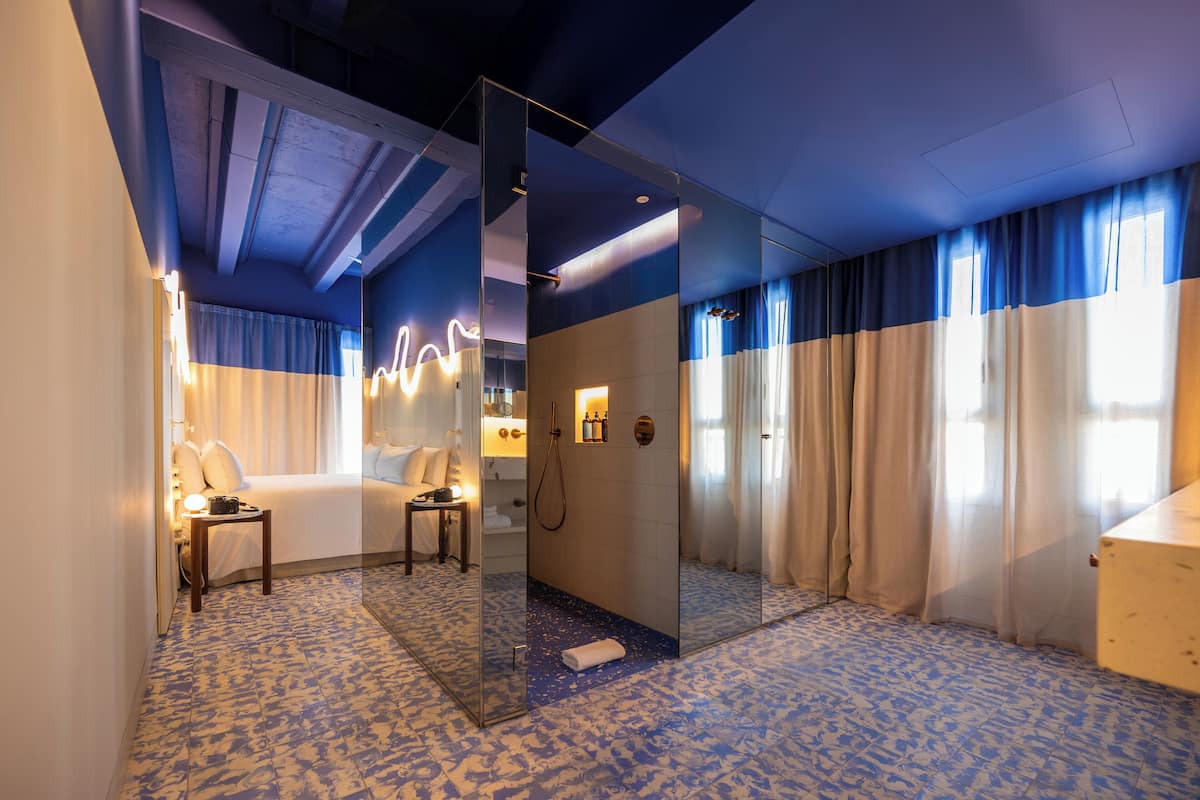 Habitación de hotel con cama, baño con ducha, espejo y suelo estampado.