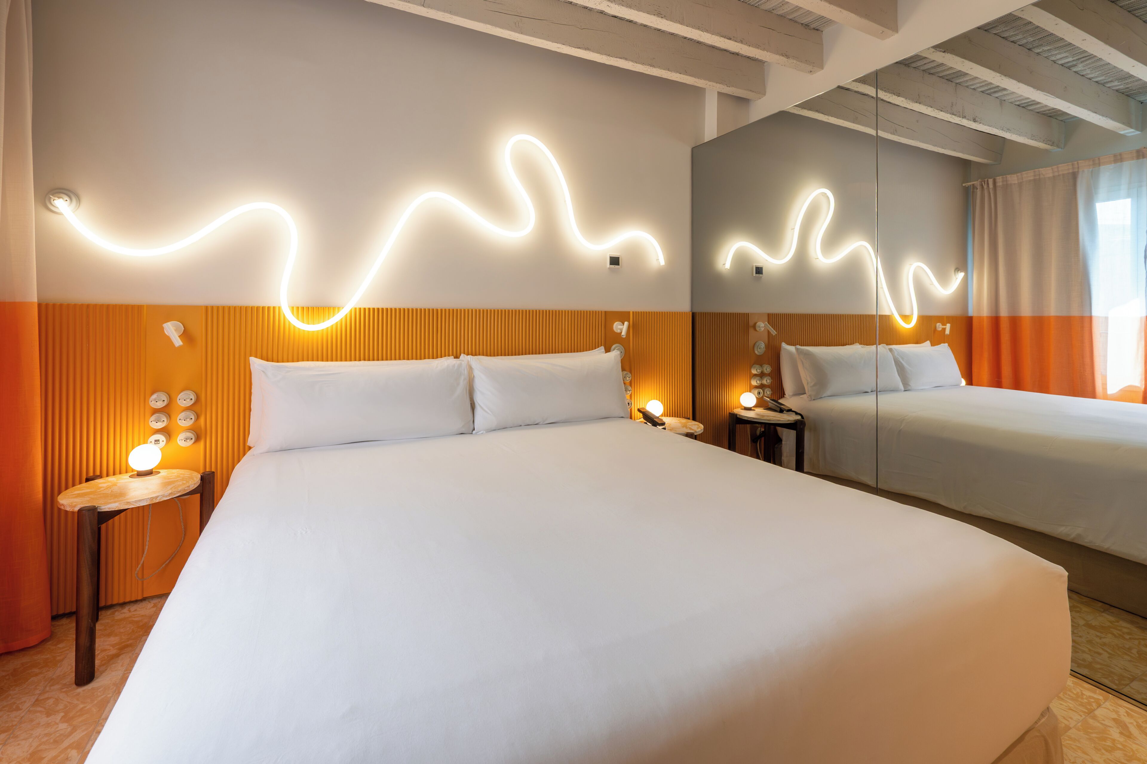 Habitación de hotel con dos camas, un espejo, una mesita de noche con lámpara y un aplique de pared.