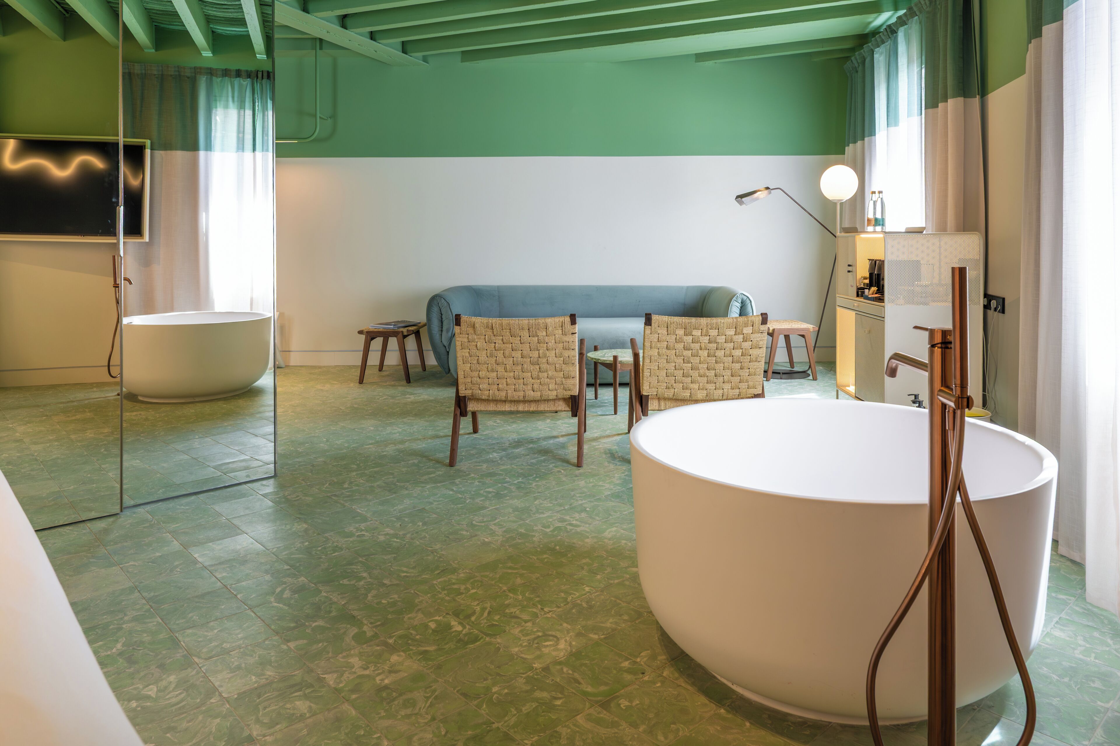 Un baño moderno con una bañera grande, dos sillones de mimbre, un sofá y un espejo.