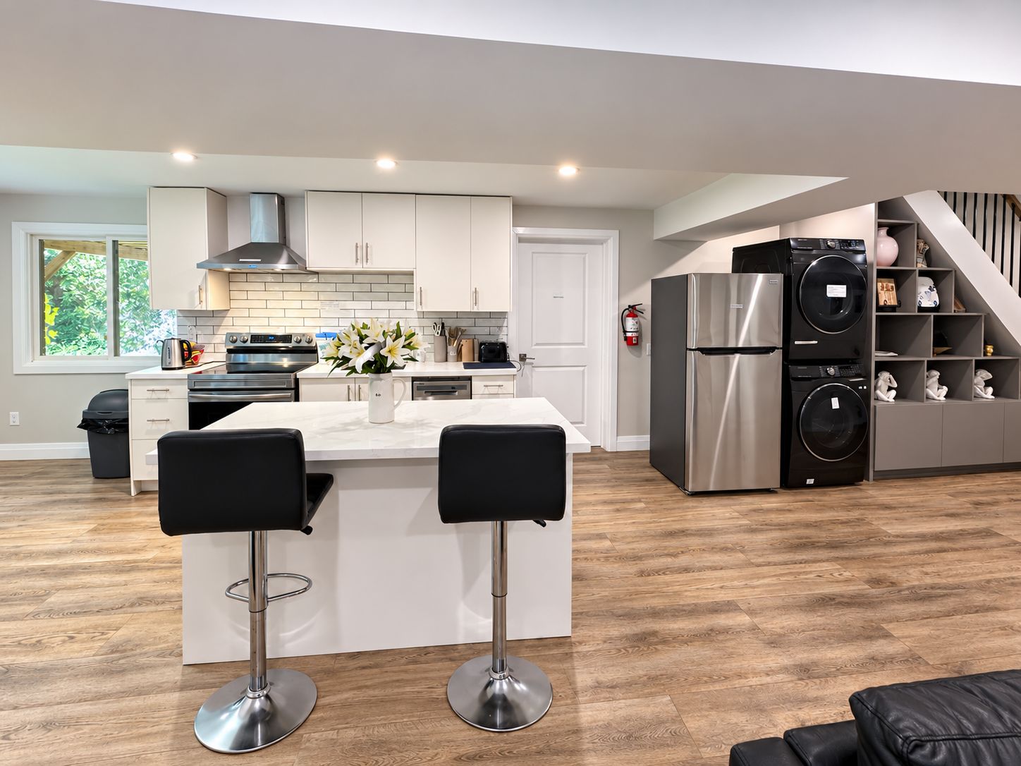 A modern kitchen with white cabinetry, stainless steel appliances, and a central island with two black bar stools.