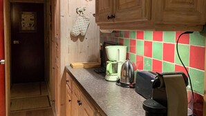 Une cuisine avec des meubles de rangement en bois, un plan de travail sur lequel se trouvent une machine à café, une bouilloire et un grille-pain, et un pare-feu en carreaux.
