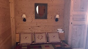Une pièce en bois avec un lit, deux lampes fixées au mur, un miroir et une porte.