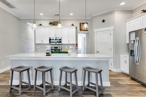 Een moderne keuken met een centraal eiland, barkrukken, witte kasten, roestvrijstalen apparatuur, hanglampen en een sterdecoratie aan de muur.