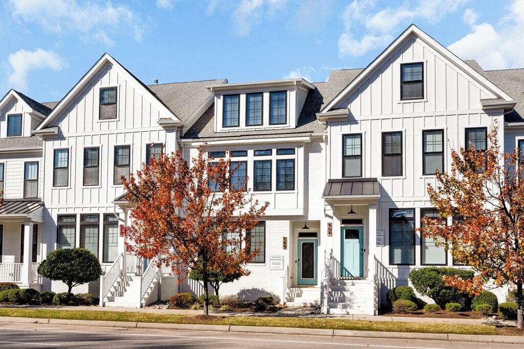 Une rangée de maisons de ville blanches, dotées d’une entrée centrale, d’un petit porche et d’un escalier menant à la porte principale.