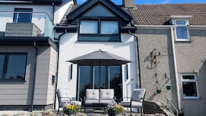 Een huis met een balkon, twee witte stoelen, een tafel en een bloempot.
