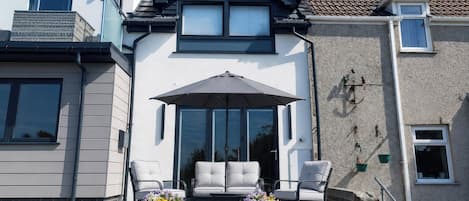 A house with a balcony, two white chairs, a table, and a potted plant.