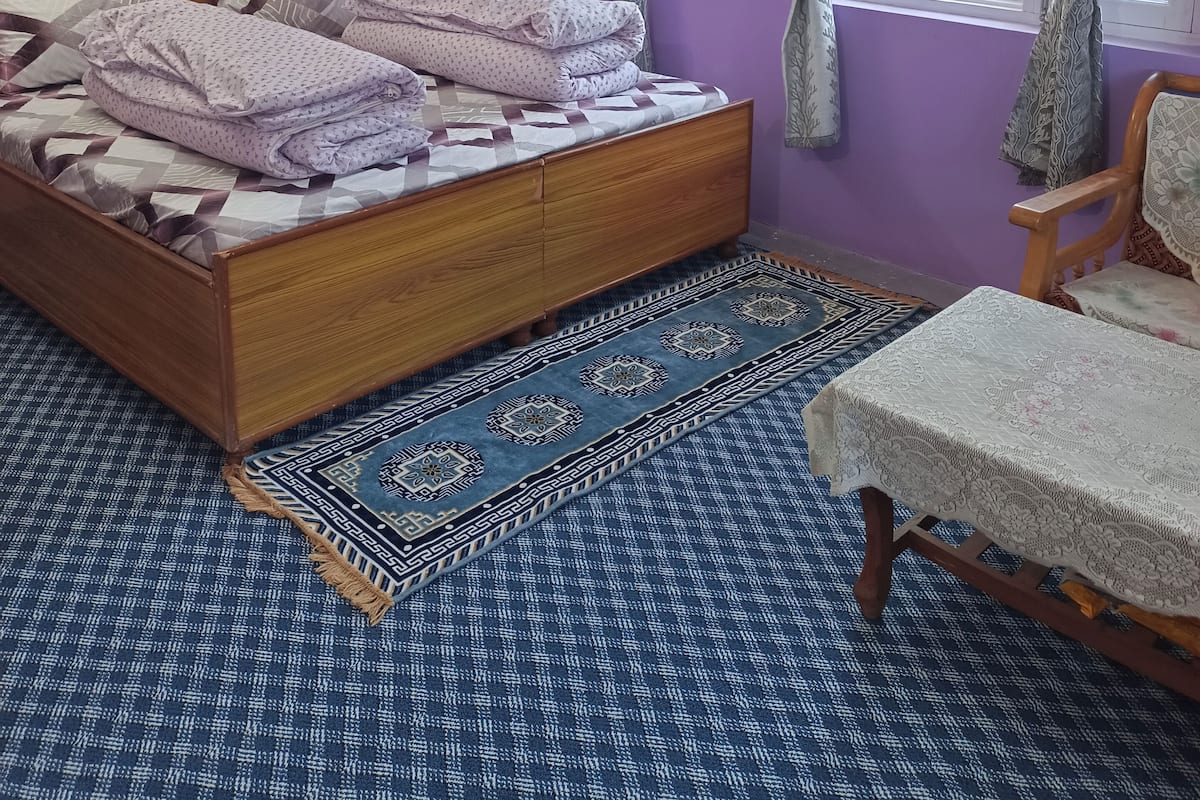 A bedroom with a wooden bed, purple walls, a window with curtains, and a patterned rug.