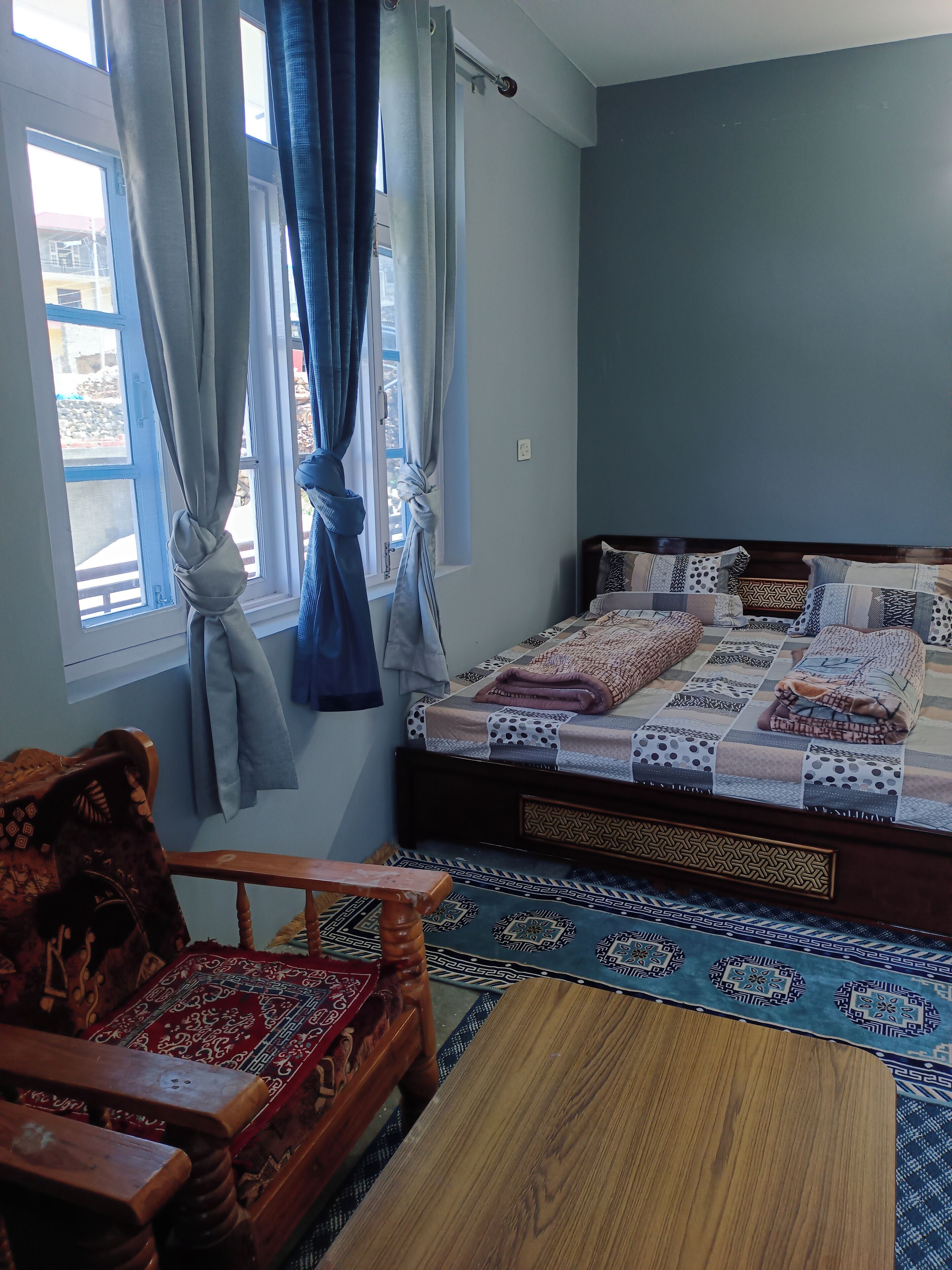 Ein Schlafzimmer mit einem Bett, einem Holzstuhl, einem kleinen Tisch und einem Fenster mit Vorhängen.