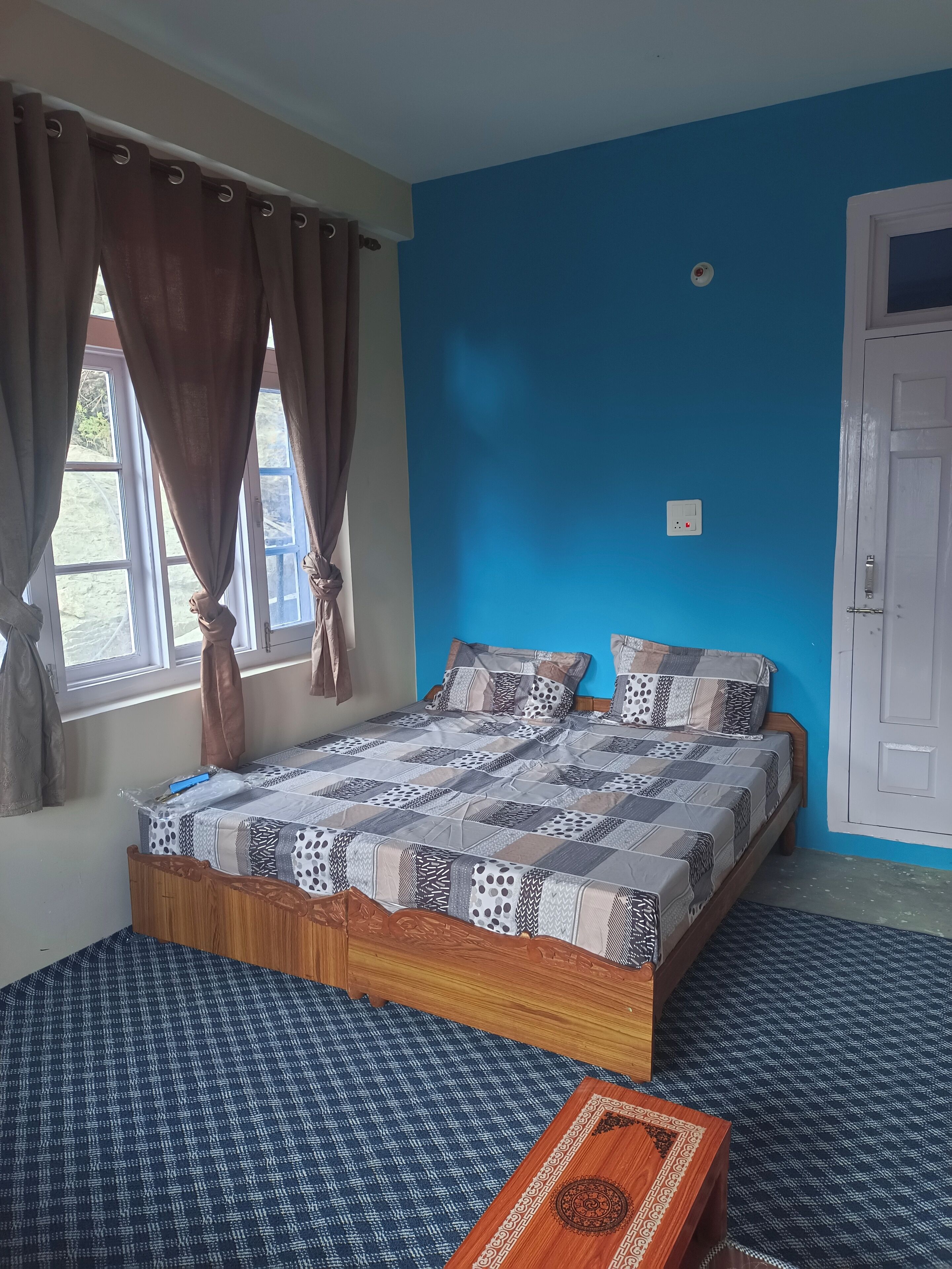 Ein Schlafzimmer mit einem großen Bett, einem Fenster mit Vorhängen, einer blauen Wand und einer Tür.