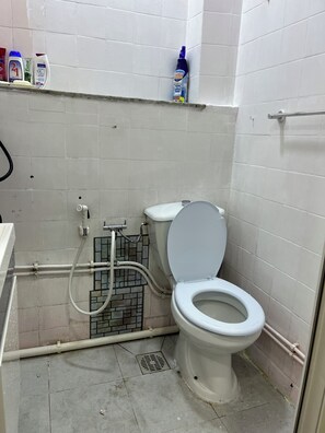 A small, tiled bathroom with a toilet, a shower, and a shelf with toiletries. - Cosy F2 apartment in the heart of Algiers (Alger Centre)